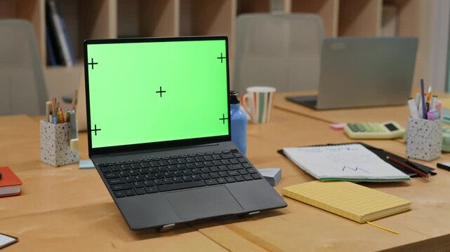 Laptop with green screen and tracking markers sitting on wooden office desk during slow pan. Footage is perfect for showcasing custom software, website design, or digital product mockups