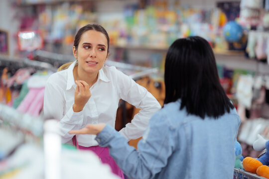 Passionate Female Shop Assistant Explaining Clothing Options To Young Customer. Enthusiastic woman worker gesturing while helping client choose garments inside retail boutique

