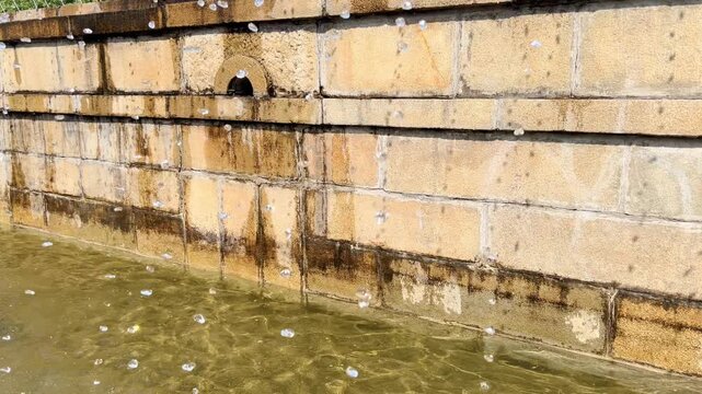 Angled view shows fountain outlet and water flowing beside stained masonry