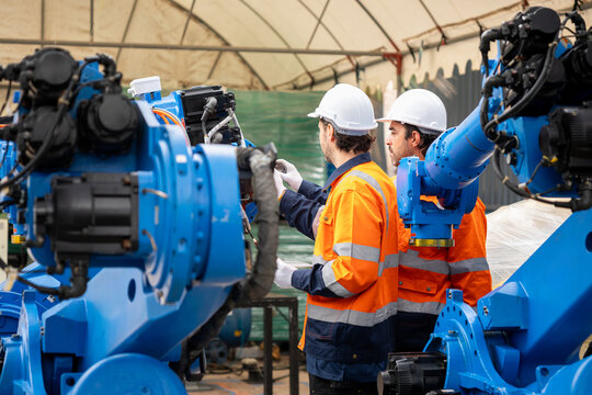 Robotics engineers team working with automated robotic arm in factory plant, automation technicians inspecting industrial robotic machinery in manufacturing facility
