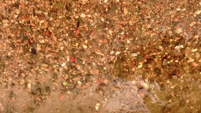 Clear river water ripples continuously above colorful gravel and sediment