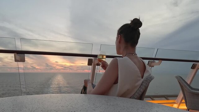 Woman drinking white wine on cruise ship deck at sunset. Looking at ocean and ship wake. Symbolizes luxury vacation and relaxation. Ideal for travel and lifestyle content