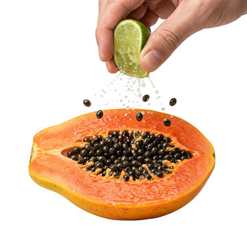 Hand squeezing lime over halved papaya with black seeds on white background.
