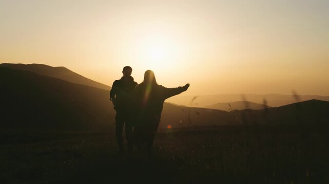 Holding hands during sunset in a valley surrounded by hills with silhouettes of a couple against the sun