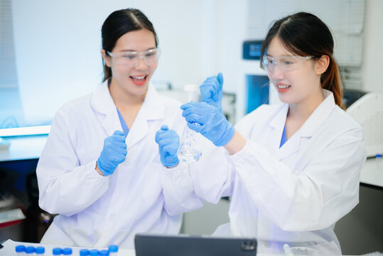 Asian female scientists conducting research with a micropipette and digital tablet in laboratory.