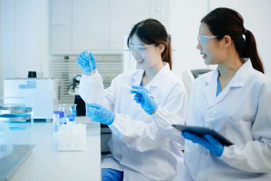 Asian female scientist holding a test tube with liquid sample during scientific research in a modern biotechnology laboratory.