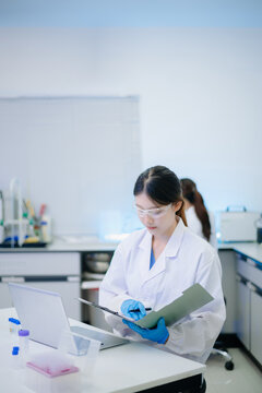 Female scientist analyzing data on laptop with chemical test tube samples in a modern biotechnology laboratory.