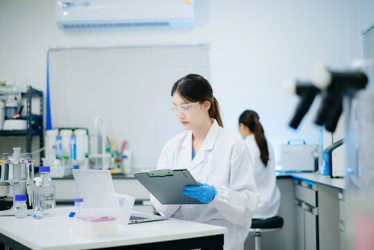 Female scientist analyzing data on laptop with chemical test tube samples in a modern biotechnology laboratory.