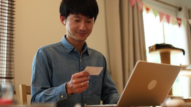 slow motion scene adult asian man hold credit card to make payment on online shopping e-commerce platform while sit in living room for people lifestyle concept