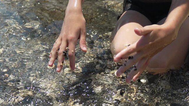 Stones sea water, woman holding small pebbles inside crystal clear ocean surf on sunny summer day relaxing vacation holiday leisure activity