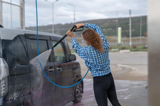 Woman pressure washing dirty black minivan at self service car wash station outdoors
