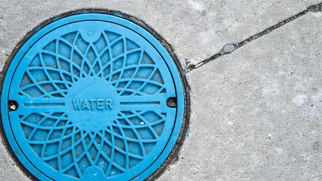 Bright blue circular water utility access cover set in gray concrete