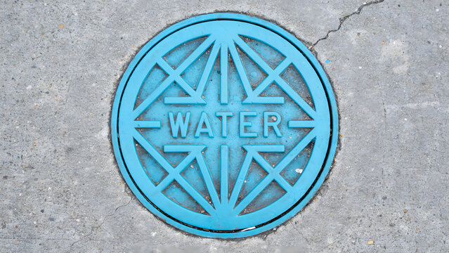 A bright blue circular water utility access cover set in concrete pavement