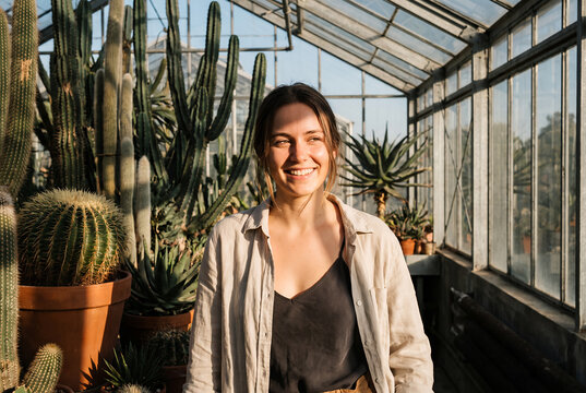 Young woman smiling in greenhouse surrounded by cacti plants