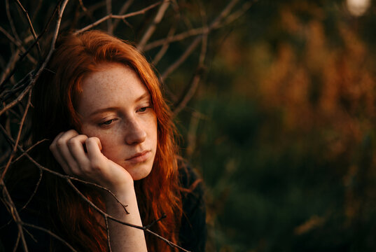 Red-haired woman contemplative among tree branches