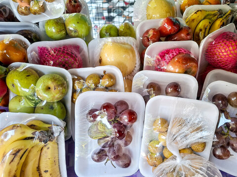 A variety of fresh, colorful fruits neatly packed in white styrofoam trays and wrapped in clear plastic film.