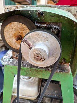 mechanical coconut grater machine showing its belt drive system, metal wheels, and green frame.
