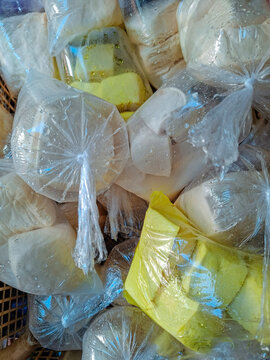 Multiple small clear plastic bags filled with white and yellow square tofu blocks stacked together.