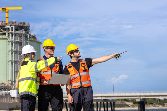 lng plant engineers team with laptop at industrial facility, liquefied natural gas plant workers discussing project outdoors, energy industry professionals inspecting storage facility with computer