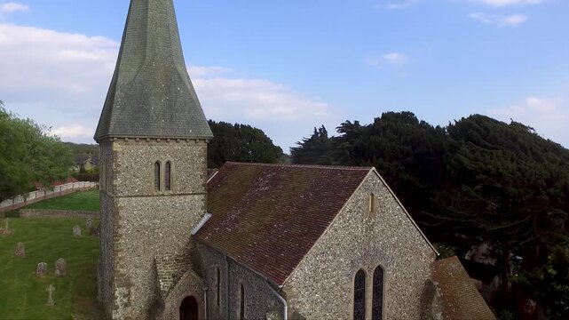 An old medieval church rising up above it to reveal green rolling hills of the English countryside, country villages and a church yard below