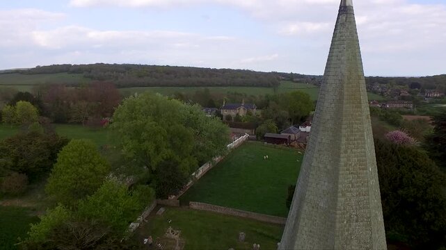 Drone shot flying up the tower of an old medieval church with a graveyard below and rolling hills in the background