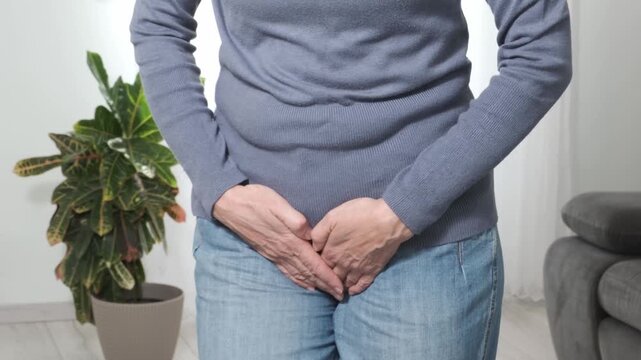 An adult woman writhes in pain in her lower abdomen, pressing her palms against the painful area. Women's problems, cystitis, bladder inflammation, fibroids, menopause, post-operative, menstrual pain