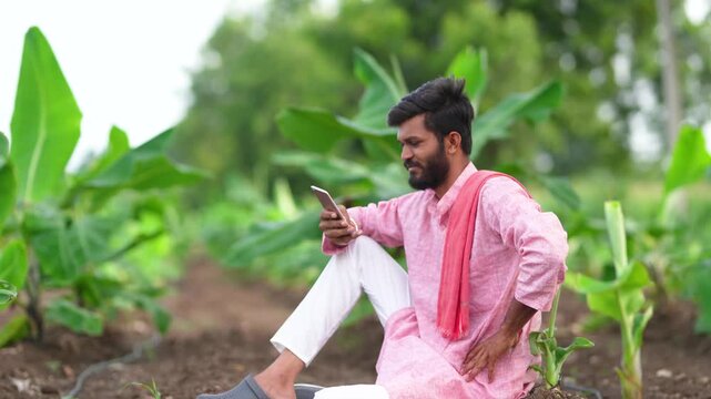 Young indian farmer sitting at banana agriculture field and using mobile phone 