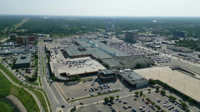 Aerial drone orbit of CF Polo Park from a different angle showcasing the shopping centre, expansive parking areas, and surrounding commercial development on a summer day