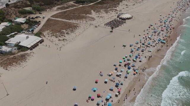 Aerial - Conil Spain sandy beach with rows of colourful umbrellas bathers and waves