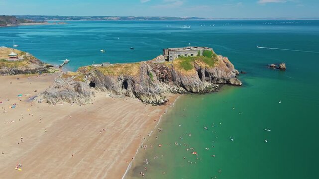 St Catherines Island and historic Palmerston fort at Tenby Castle Beach, Pembrokeshire, Wales, holidaymakers swimming in calm turquoise sea below rugged coastal cliffs