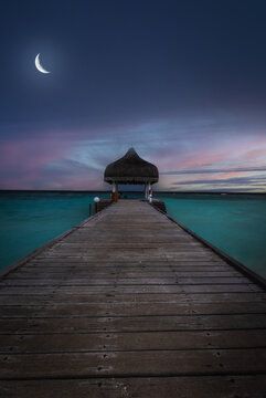 Wooden jetty under a crescent moon at twilight in the Maldives