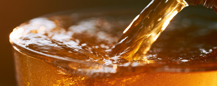 Kombucha is being poured into a glass indoors with bright backlighting at evening