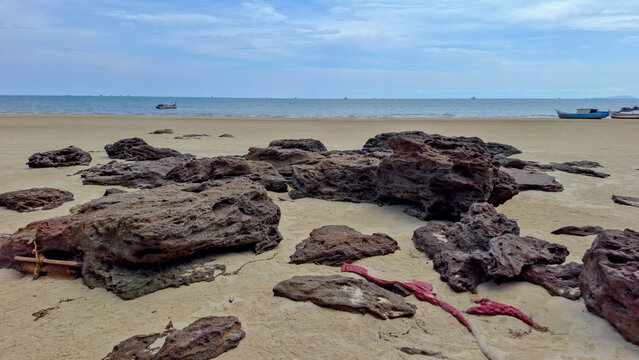 Wide view of flat weathered rock formations embedded in the sand along a beach coast looking out towards a calm ocean horizon.