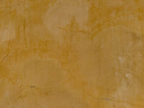 The old, mustard-yellow plastered wall surface, with its hairline cracks and dark stains from age, is ideal for use as a backdrop or in vintage, loft, and industrial-style designs
