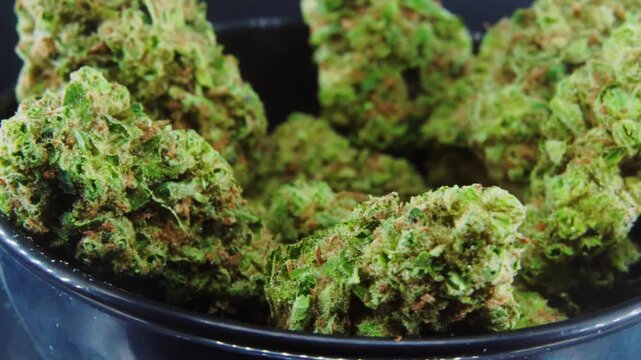 Close up rotation of several marijuana buds or cannabis flower in small black bowl against black background.