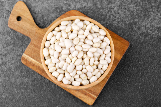 White beans in wooden bowl on cutting board for rustic cooking, vegan ingredient or healthy kitchen concept