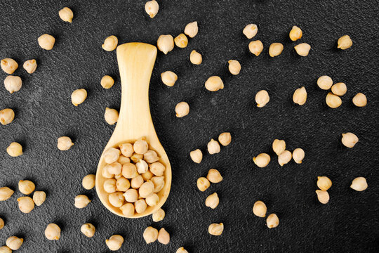 Scattered chickpeas and wooden spoon on dark background for food design, protein source or vegan diet concept