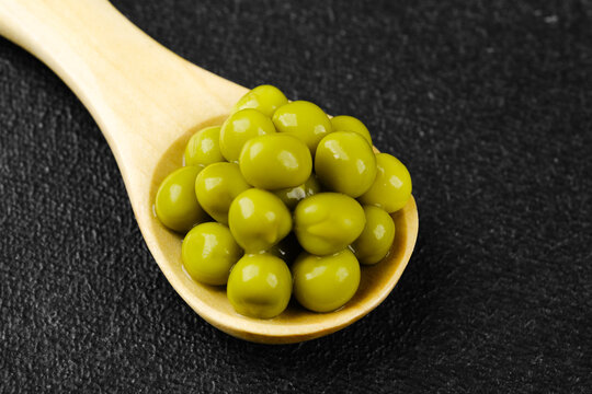 Small wooden spoon with green peas on dark stone surface for organic ingredient, diet or cooking concept