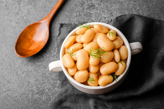 white beans in tomato sauce with herbs in white bowl on gray background for clean eating, comfort food or healthy lunch concept