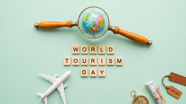 World Tourism Day concept, vintage magnifying glass with globe, wooden Scrabble letters, airplane model, and travel accessories on a pastel green background