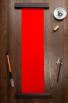 Blank red Chinese couplet rice paper scroll mockup on dark wooden background with ink brushes and seals top view