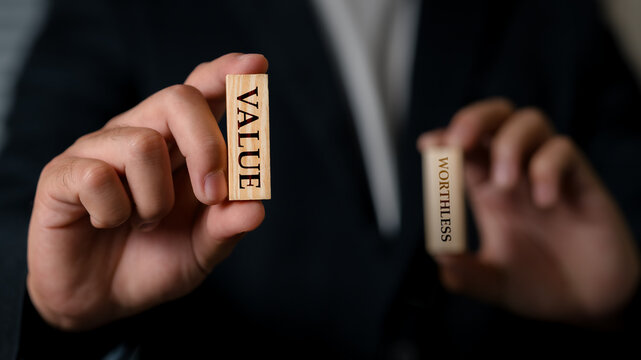 Close-up of a business person holding two wooden blocks with Value and Worthless written on them, symbolizing contrasting business or financial concepts.