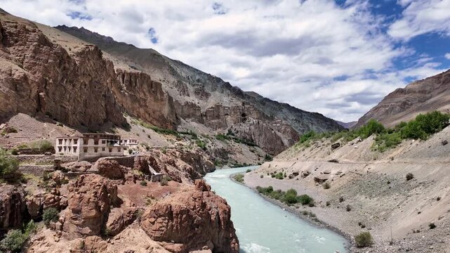 Zanskar, India : Tilt down footage of tsarap river in Lungnak valley with the ancient Phuktal gompa in the background, cliffside monastery built in natural cave of Zanskar in Ladakh, India