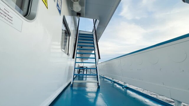 A cruise ship stair stairs leads upward as the vessel sails across Lake Ladoga. Soft sunlight shines through the blue deck under a peaceful sky. This calm voyage brings a feeling of quiet wonder and j