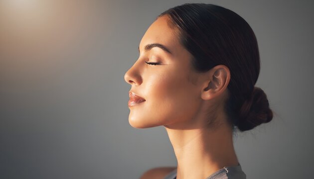 Retrato de perfil de mujer joven con ojos cerrados y cabello recogido sobre fondo neutro con iluminaci&oacute;n suave