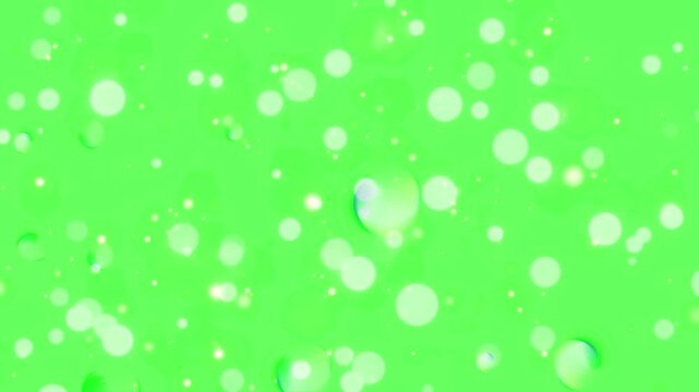 Particles of glowing light floating across a vibrant green screen backdrop form a dynamic abstract pattern.