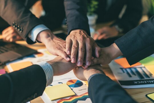 Close up of diverse business team stacking hands together over a desk with charts and documents