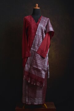 Maroon embroidered kebaya with songket skirt and shawl displayed on a dress form