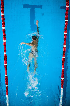 Top view of swimmer doing freestyle front crawl toward pool wall, arm extended forward with splashing water. Concept of progress, direction, ambition and reaching target