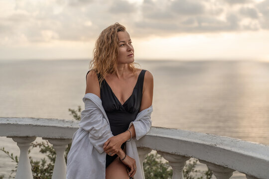 Woman leaning on terrace railing enjoying tranquil ocean view during late afternoon light